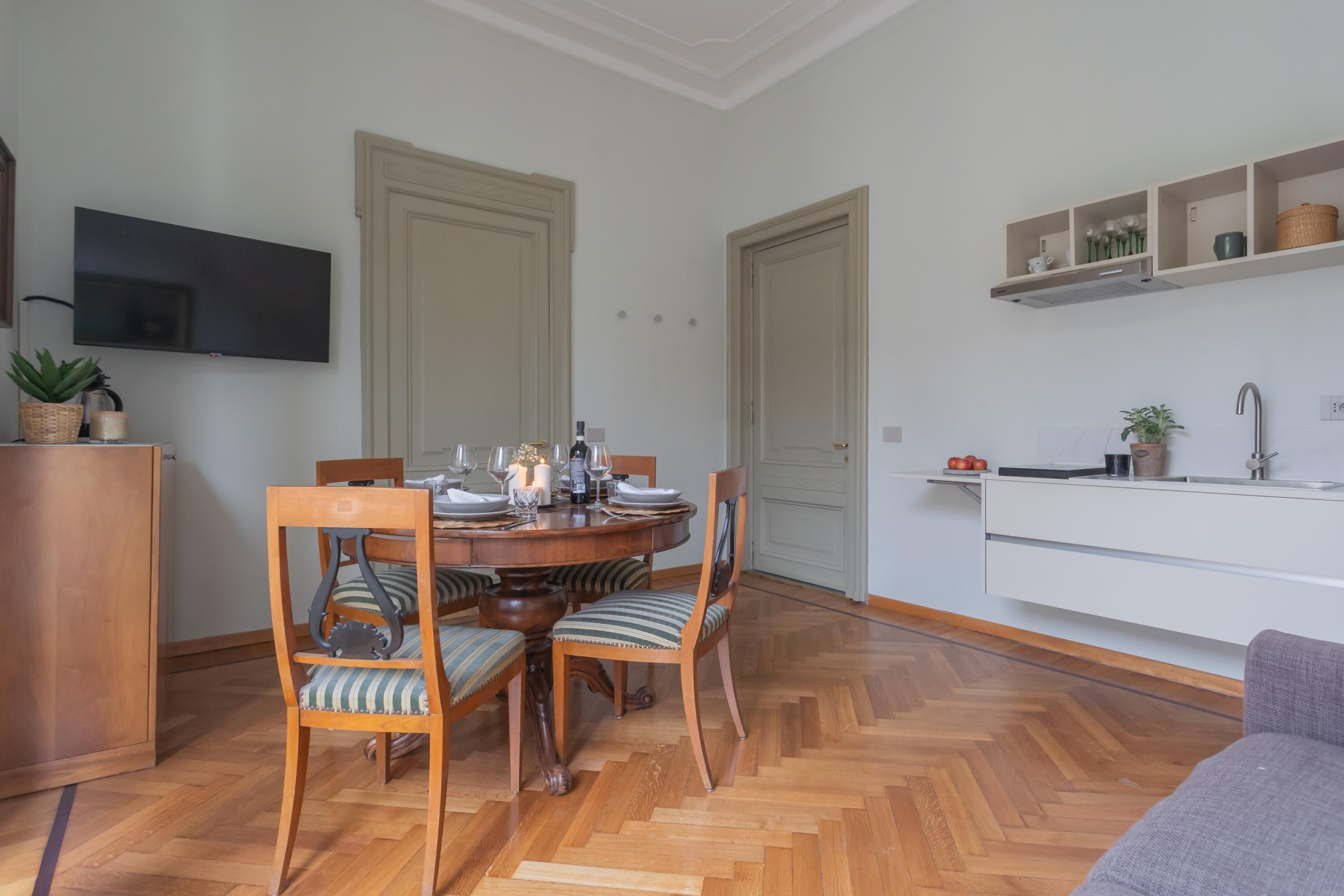 A dining area with a round table, chairs, and a television mounted on the wall.
