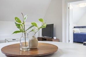 A modern room with a bed, a TV, and a wooden table with two vases of plants.