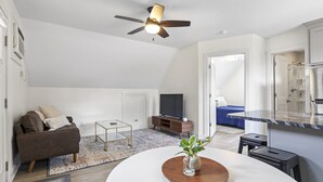 Ein geräumiger Wohnbereich mit Deckenventilator, Fernseher, Sofa, Couchtisch und einer Küchenzeile mit Arbeitsplatte und Schränken.