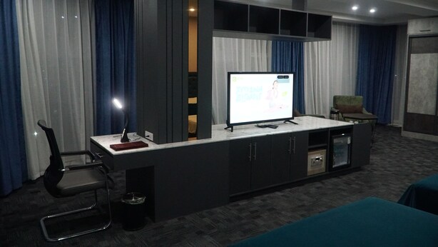 A modern hotel room with a large TV, a desk with a chair, a sofa, and a minibar. - Bayantsambagarav Hotel (Olgii)