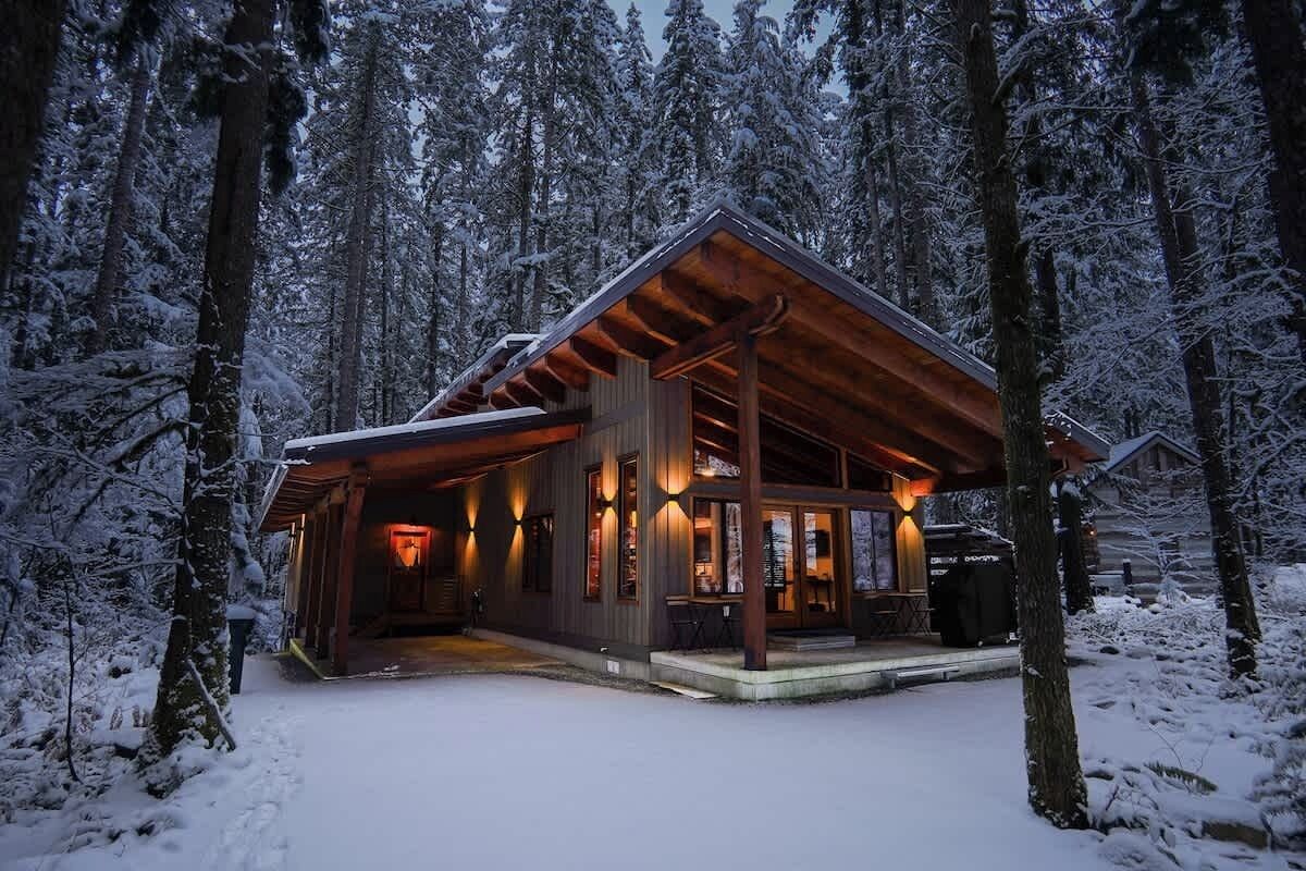 Une cabane en bois dotée d’un porche, entourée d’arbres couverts de neige.