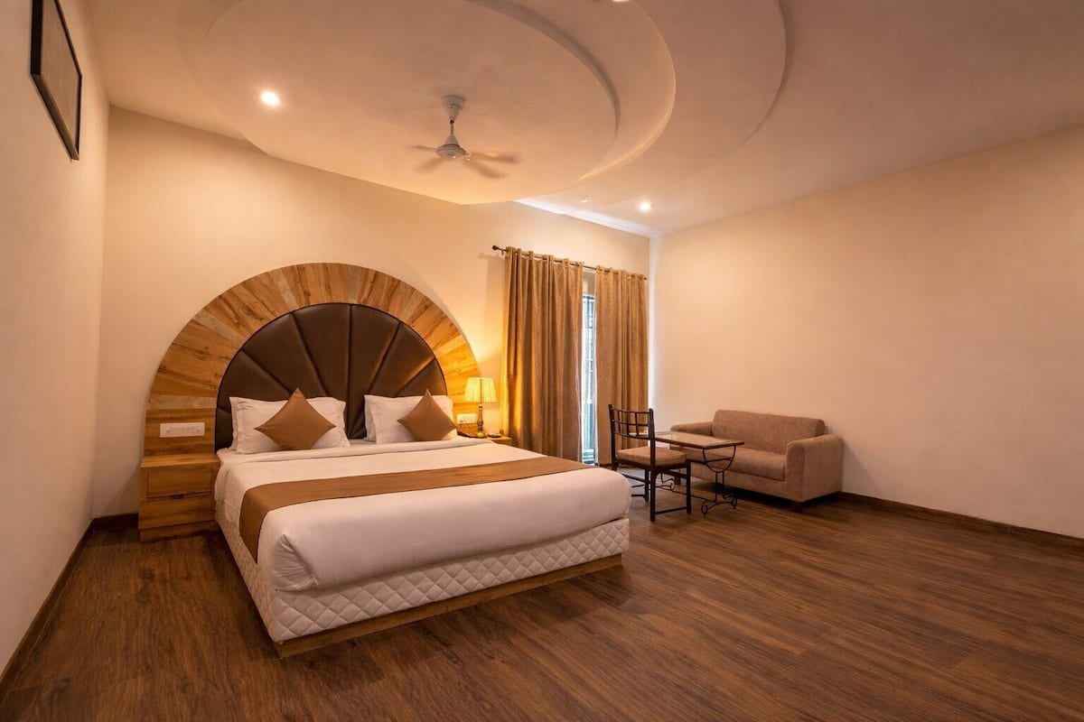 A hotel room with a bed, a chair, a table, a ceiling fan, and a window with curtains.