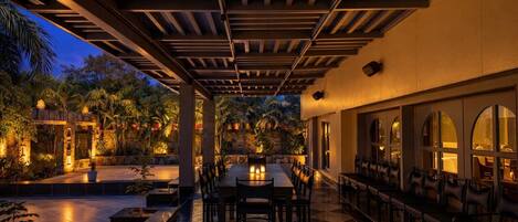 An outdoor dining area with a checkered floor, wooden pergola, and tables with chairs.