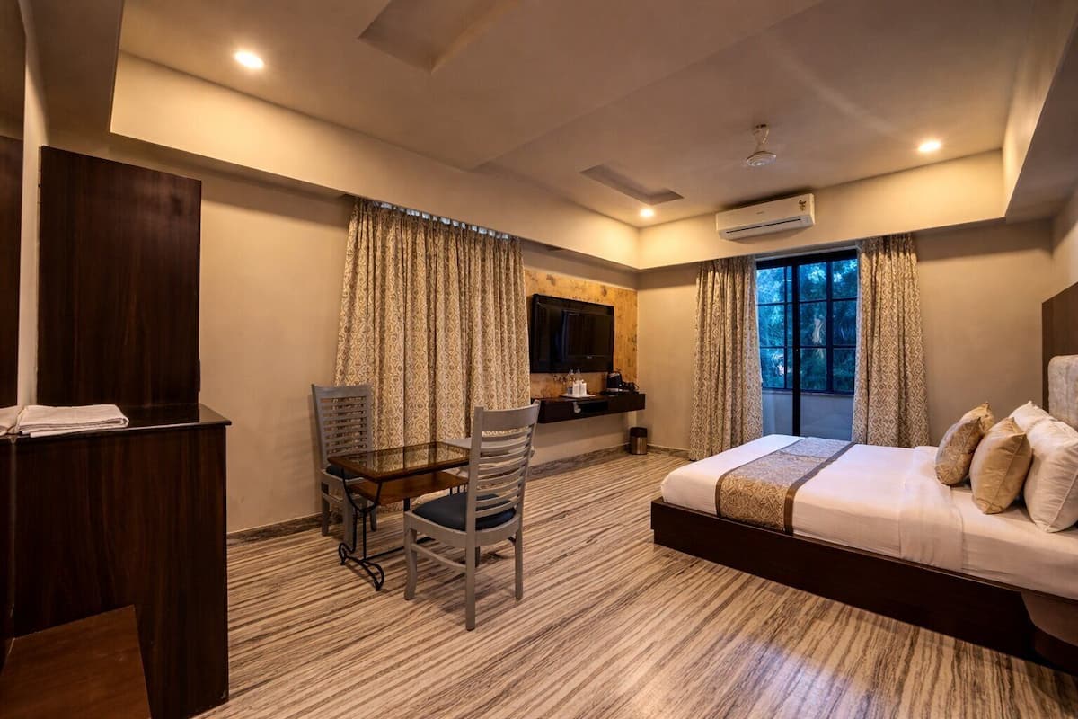 A hotel room with a bed, a desk, a chair, a TV, and a window with curtains.