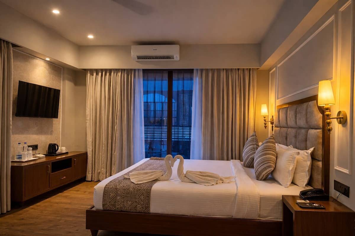 A hotel room with a bed, bedside lamps, a TV, a desk with a phone, and a window with curtains.