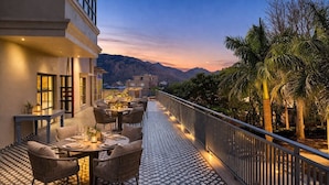 An outdoor dining area with tables and chairs, a patterned floor, and a view of mountains and palm trees. - Devi Palace Monsoon Palace View Resort Udaipur (Udaipur)