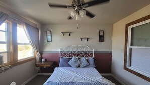 Ein Schlafzimmer mit Bett, Deckenventilator, Fenster mit Vorhängen und Nachttisch.