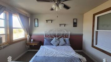 A bedroom with a bed, a ceiling fan, a window with curtains, and a bedside table.