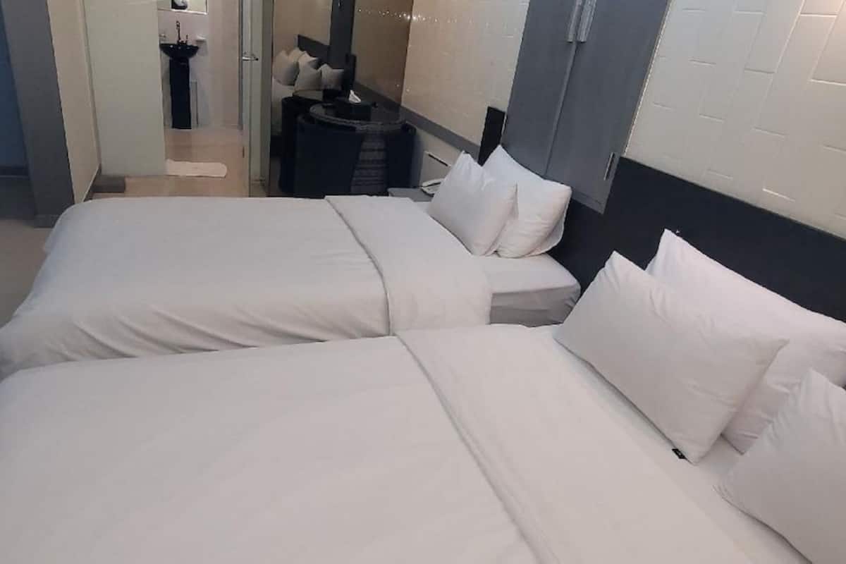 Una habitació d'hotel amb dos llits, una taula de nit petita, un mirall i vista al passadís.