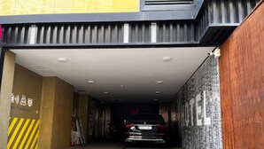 A car parked in a covered parking area with a tiled floor and a yellow and black striped wall on the left. - sinchon Y hotel (Seoul)