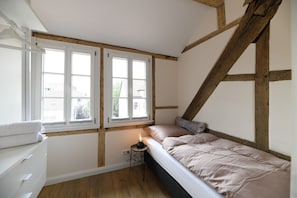 Ein Schlafzimmer mit einem Bett, einem Nachttisch, einem Fenster und Holzbalken.