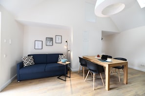 Ein modernes Wohnzimmer mit einer Couch, einem Esstisch mit Stühlen, einer Lampe und gerahmten Bildern an der Wand.