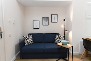 Ein Zimmer mit einem dunkelblauen Sofa, gemusterten Kissen, einem kleinen Tisch mit einer Schale und drei gerahmten Bildern an der Wand.