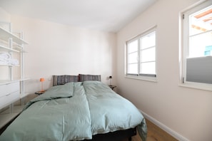 Ein Schlafzimmer mit einem Bett, einem Nachttisch, einer Lampe und einem Fenster.