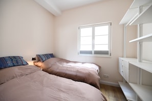 Une chambre avec deux lits, une fenêtre et des étagères intégrées.