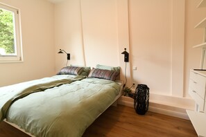 Une chambre à coucher avec un lit, des lampes de chevet, une fenêtre et une commode blanche.
