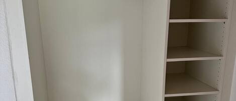 A white walk-in closet with open shelves and a metal rod for hanging clothes.