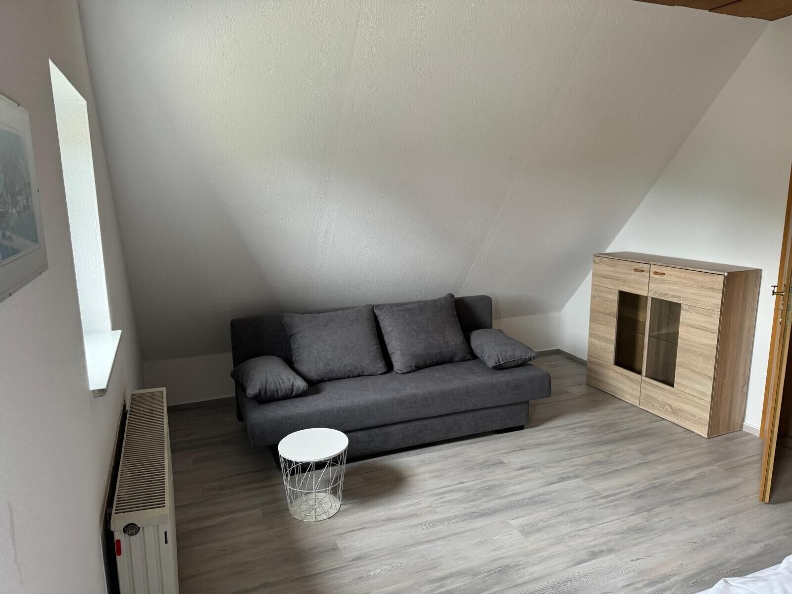 A modern loft bedroom with a grey sofa, a wooden cabinet, and a white radiator.