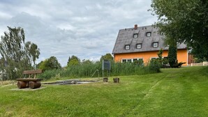 A grassy outdoor area with a wooden bench, a small pond, and a house with a sloped roof. - Apartment 'Ferienwohnung Auf Der Heide' with Shared Terrace, Shared Garden and Wi-Fi (Großschönau)