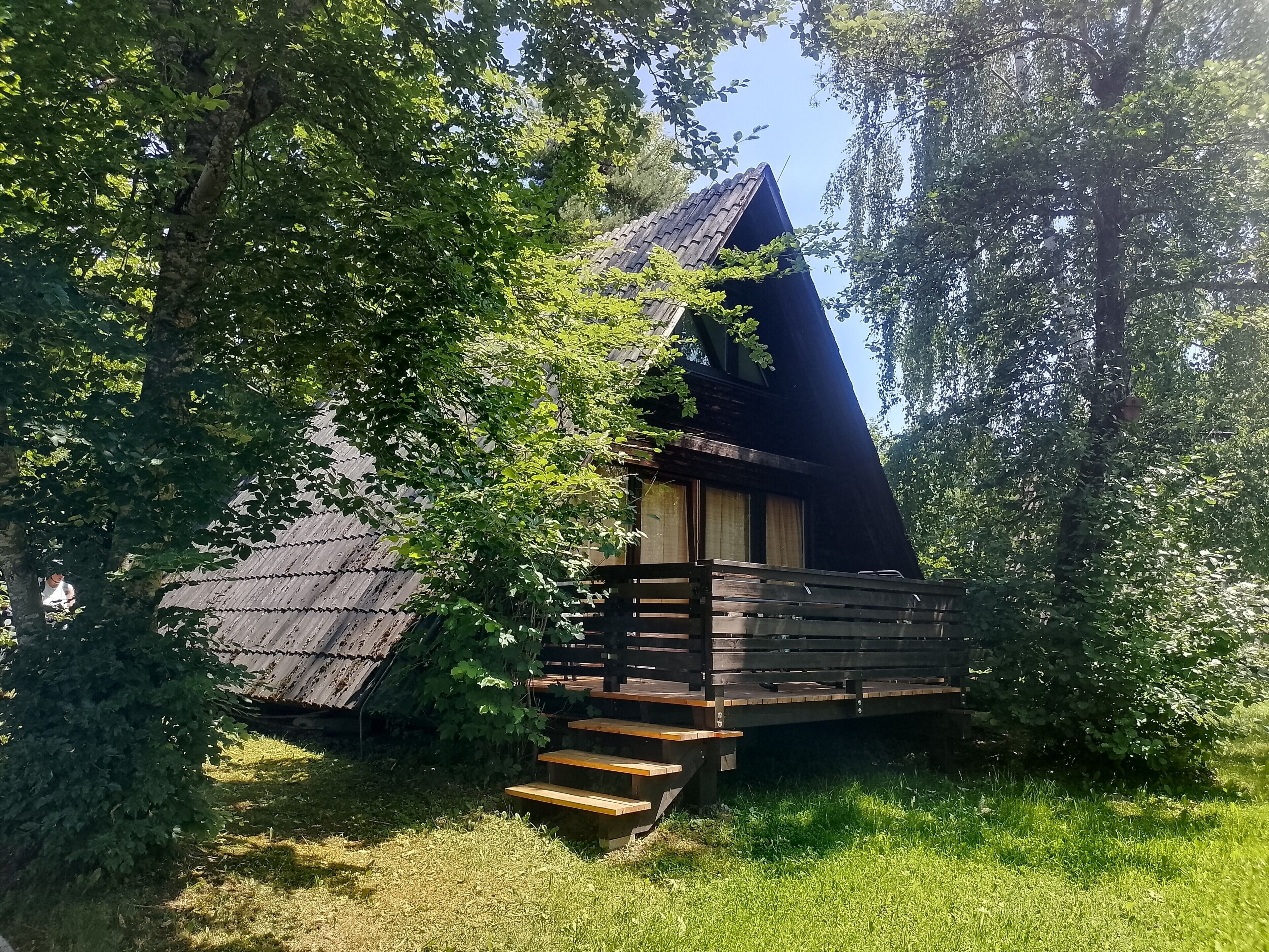 A small, triangular wooden cabin surrounded by trees.