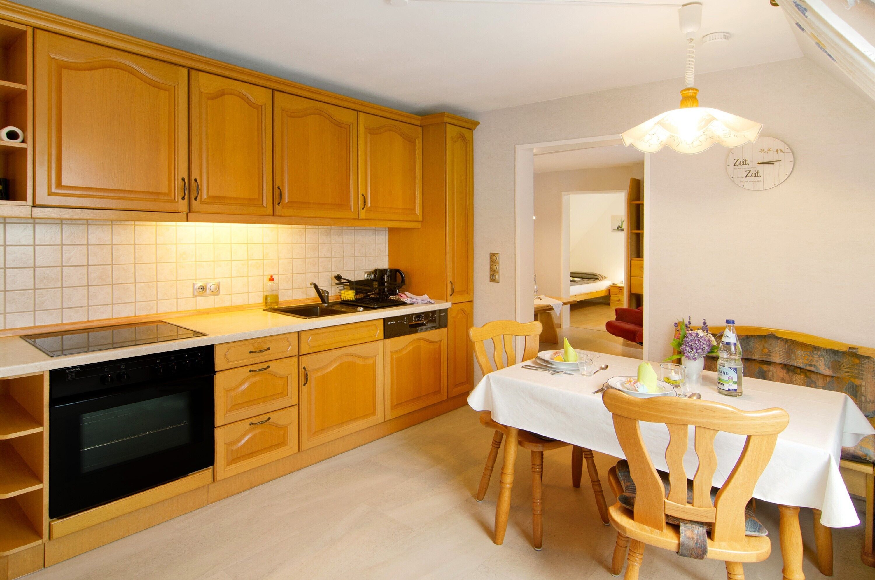 Een keuken met houten kastjes, een fornuis en een eettafel met stoelen.