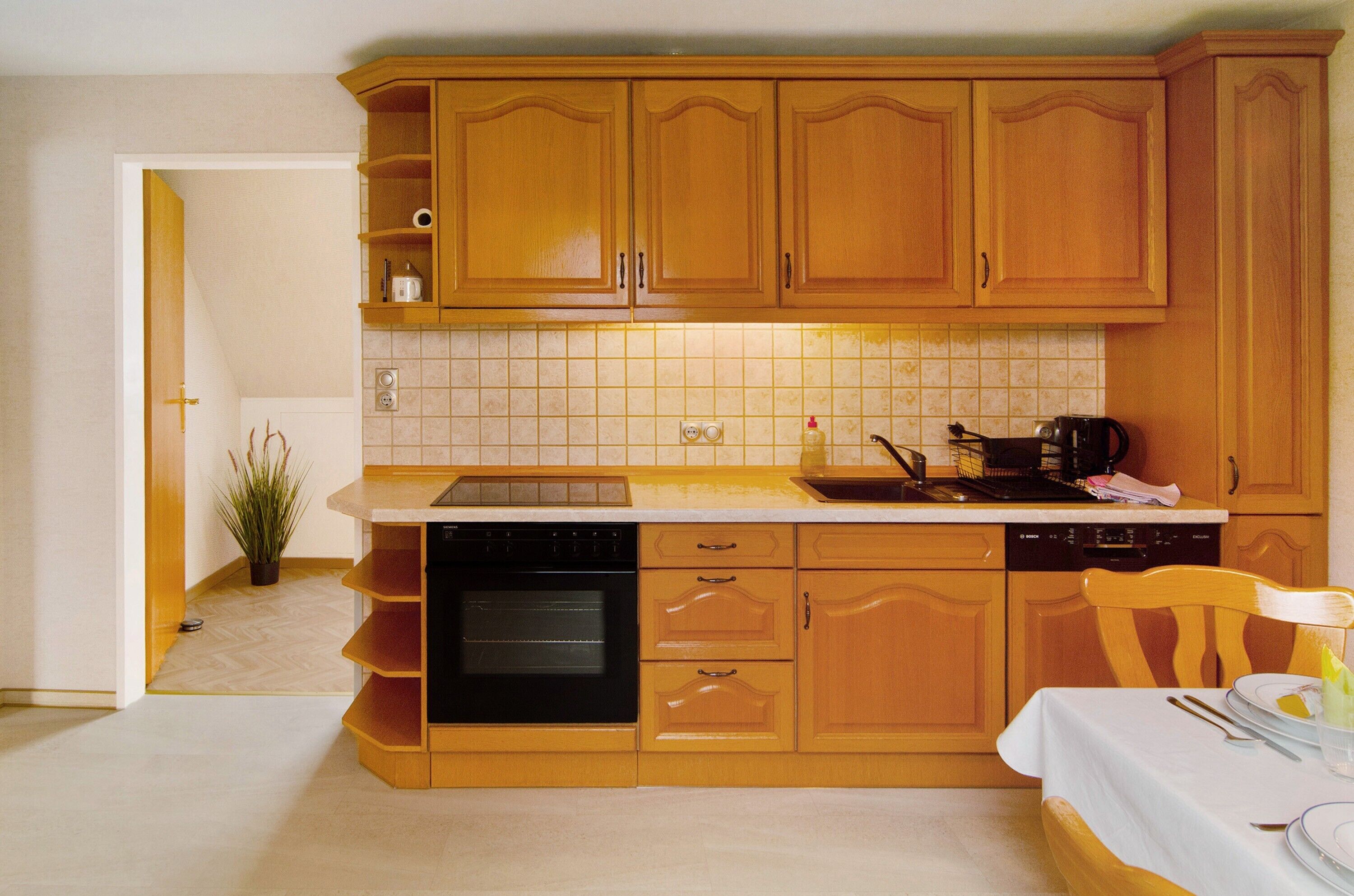Una cucina con mobili in legno, lavastoviglie, forno e zona pranzo con tavolo apparecchiato per due.