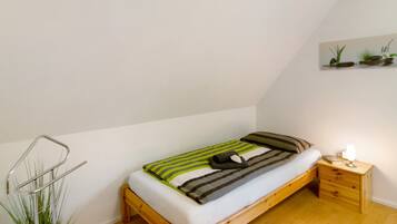 A single bed with a wooden frame, a bedside table with a lamp, and a wall-mounted shelf with plants.