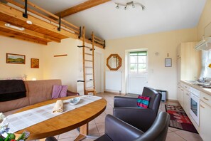 Un espace de vie chaleureux avec une table en bois, un canapé, un fauteuil, une échelle et, au fond, une cuisine.