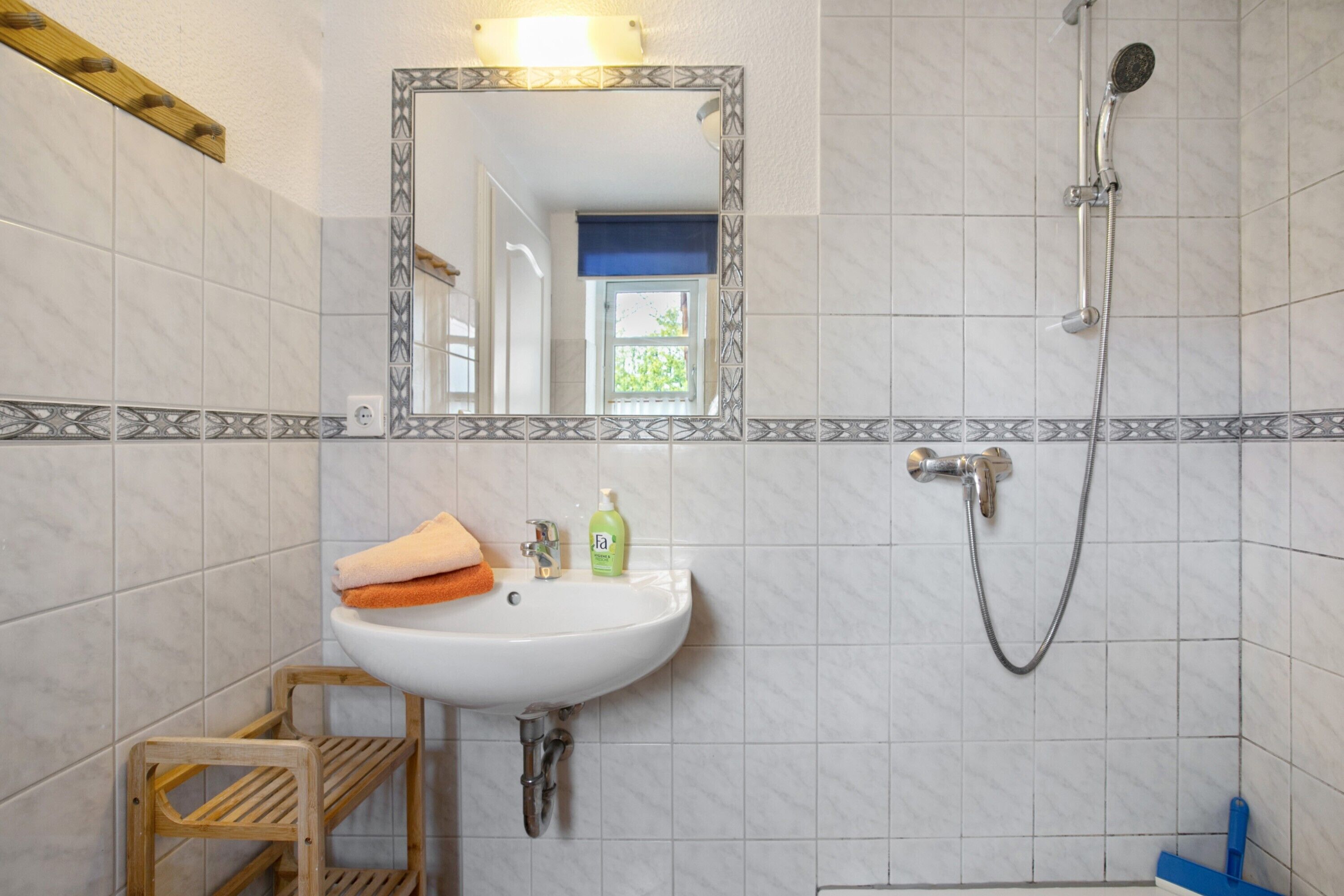 Un baño con lavamanos blanco, espejo, ducha y ventana.