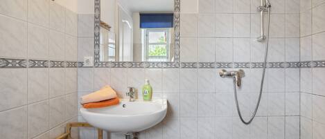 Un baño con lavamanos blanco, espejo, ducha y ventana.