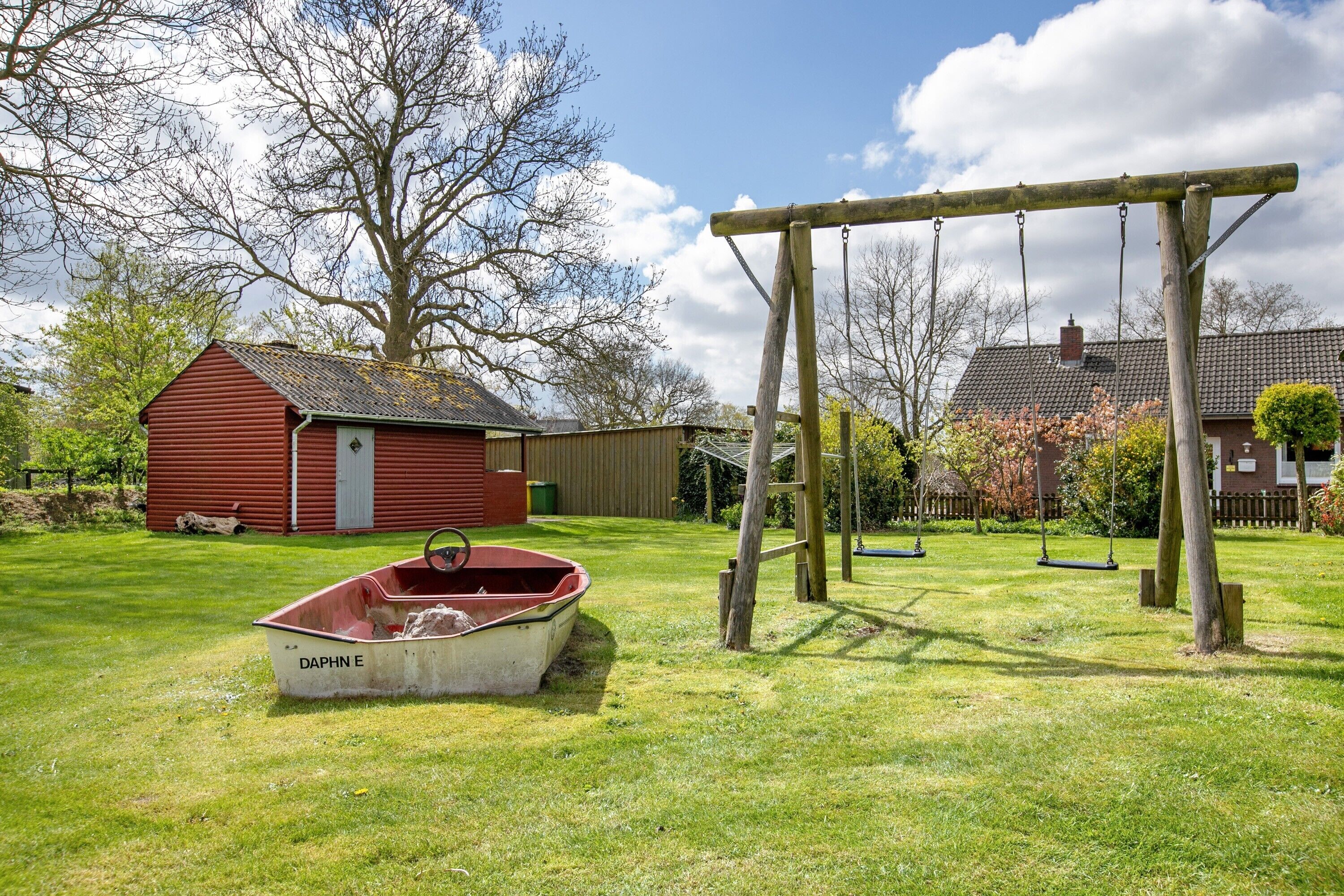A grassy yard with a swing set, a red barn, and a boat labeled 'DAPHN E' in the foreground.