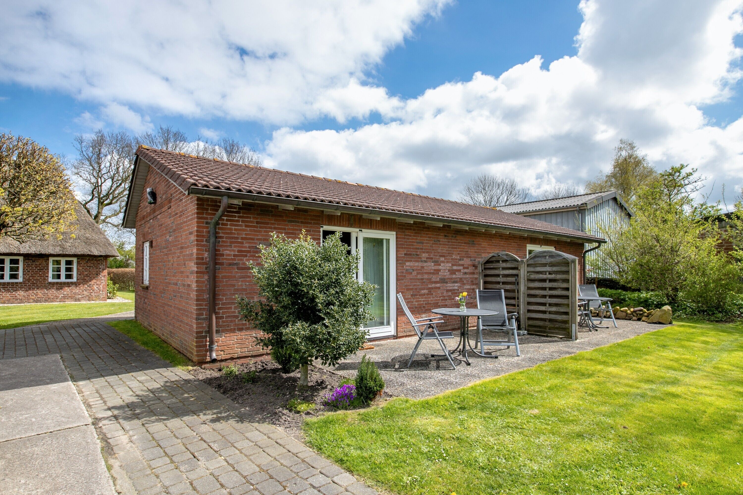 A brick house with a tiled roof, a small garden, and a patio with outdoor furniture.