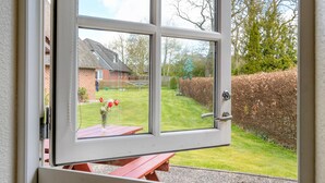 Una ventana con vista a un jardín trasero, un banco de madera y una casa.