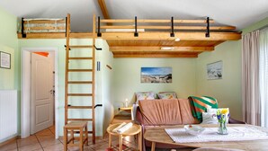A cozy room with a loft bed, a wooden ladder, a sofa, a small table, and a vase with flowers. - Apartment 'Eulenhof 1' with Private Terrace, Private Garden and Wi-Fi (Bordelum)
