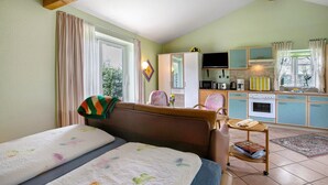 A room with two beds, a kitchenette, a TV, and a window with curtains. - Apartment 'Eulenhof 1' with Private Terrace, Private Garden and Wi-Fi (Bordelum)