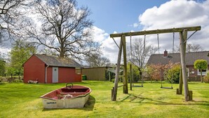A grassy yard with a swing set, a red building, and a boat labeled 'DAPHN E' in the foreground. - Apartment 'Eulenhof 1' with Private Terrace, Private Garden and Wi-Fi (Bordelum)
