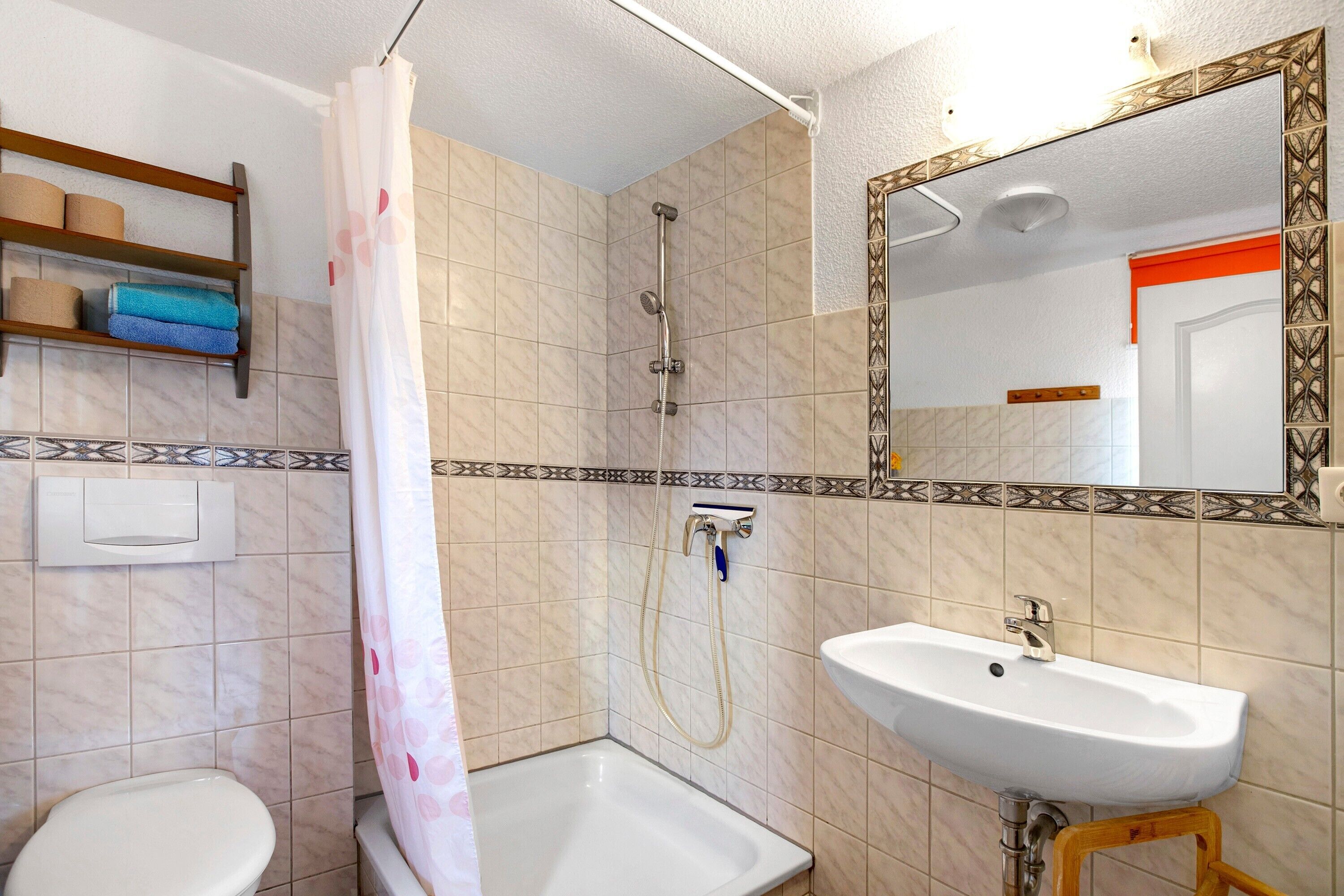 A bathroom with a shower, toilet, sink, and a mirror with a decorative frame.
