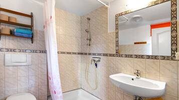 A bathroom with a shower, toilet, sink, and a mirror with a decorative frame.