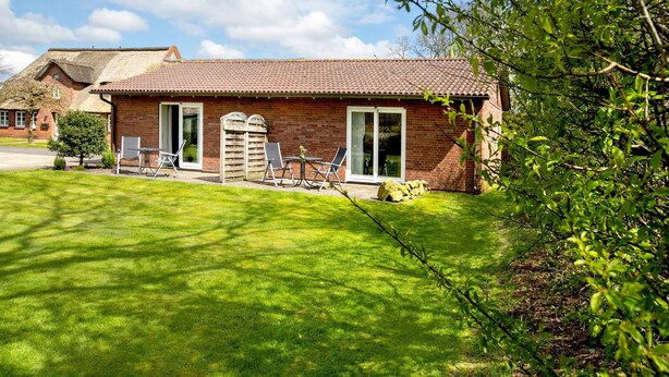 A brick house with a tiled roof, a lawn, and a small patio with outdoor furniture. - Apartment 'Eulenhof 1' with Private Terrace, Private Garden and Wi-Fi (Bordelum)