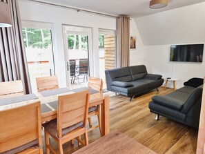 Moderni olohuone, jossa on sohva, ruokapöytä, tuoleja ja televisio.