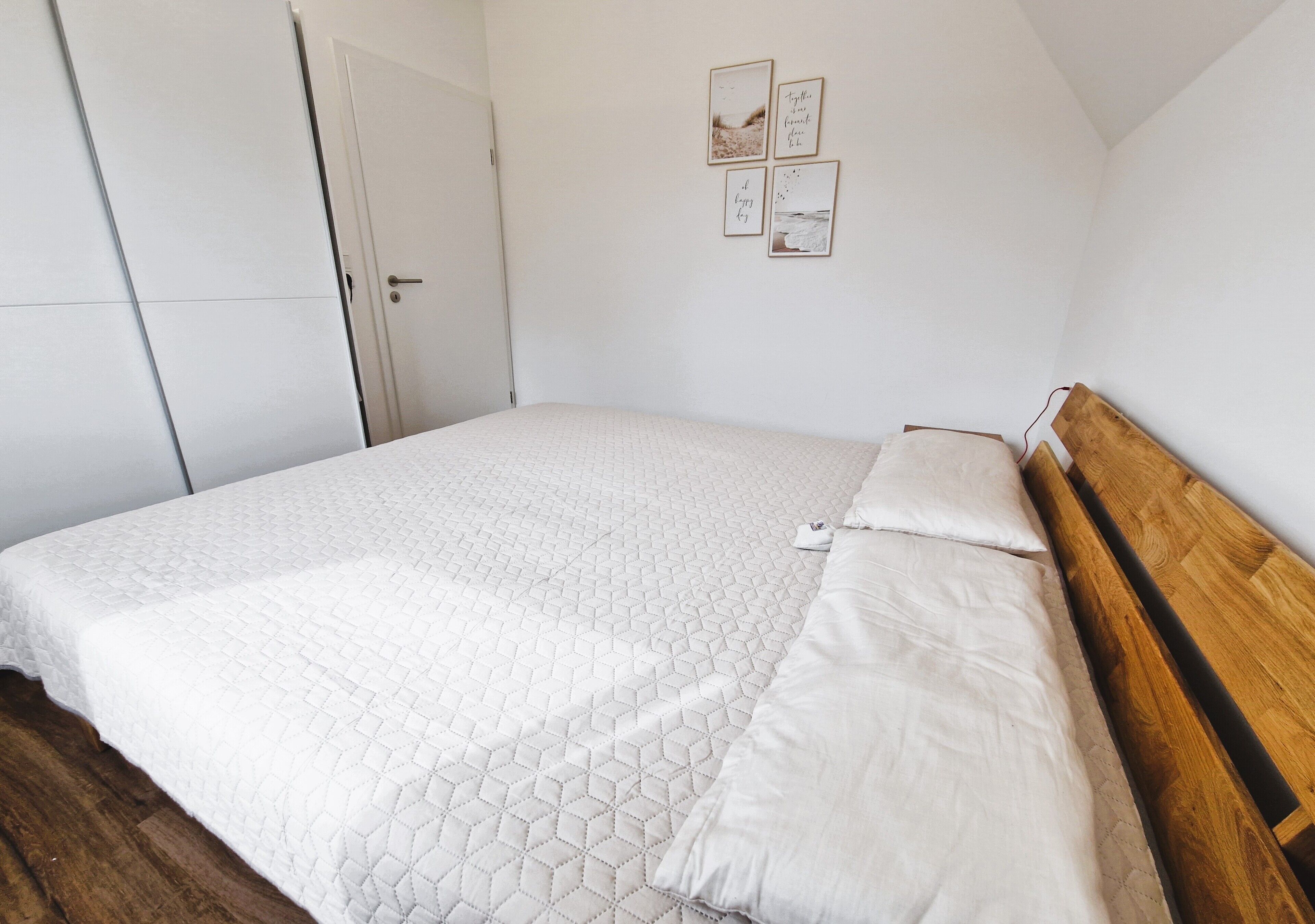 Un dormitorio con cama, cabecera de madera, paredes blancas y una puerta.