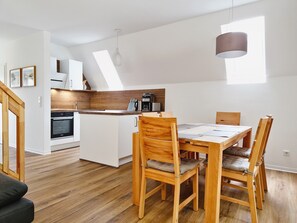 Una cucina moderna con mobili bianchi, un piano di lavoro in legno e un'area pranzo con tavolo e sedie in legno.