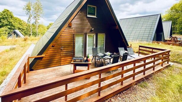 Una cabaña de madera triangular con terraza y zona de estar al aire libre.