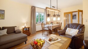 A living room with a sofa, a dining table, a leather chair, and a fruit bowl. - Apartment 'Hönneblick' with Private Terrace, Private Garden and Wi-Fi (Balve)