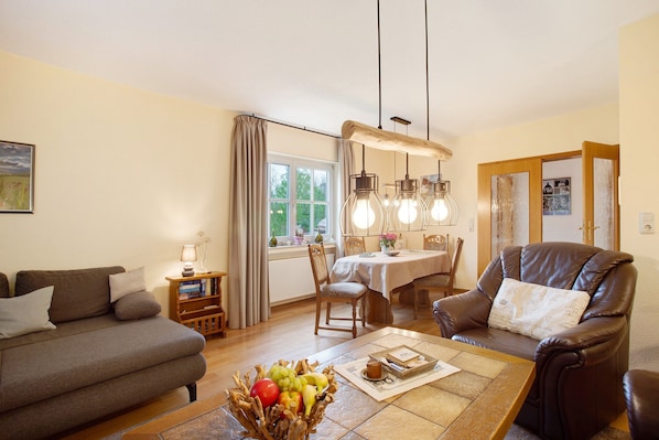 A living room with a sofa, a dining table, a leather chair, and a fruit bowl.