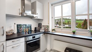 A modern kitchen with white cabinets, a black countertop, a built-in oven, and a window with a view of greenery. - Apartment 'Hönneblick' with Private Terrace, Private Garden and Wi-Fi (Balve)