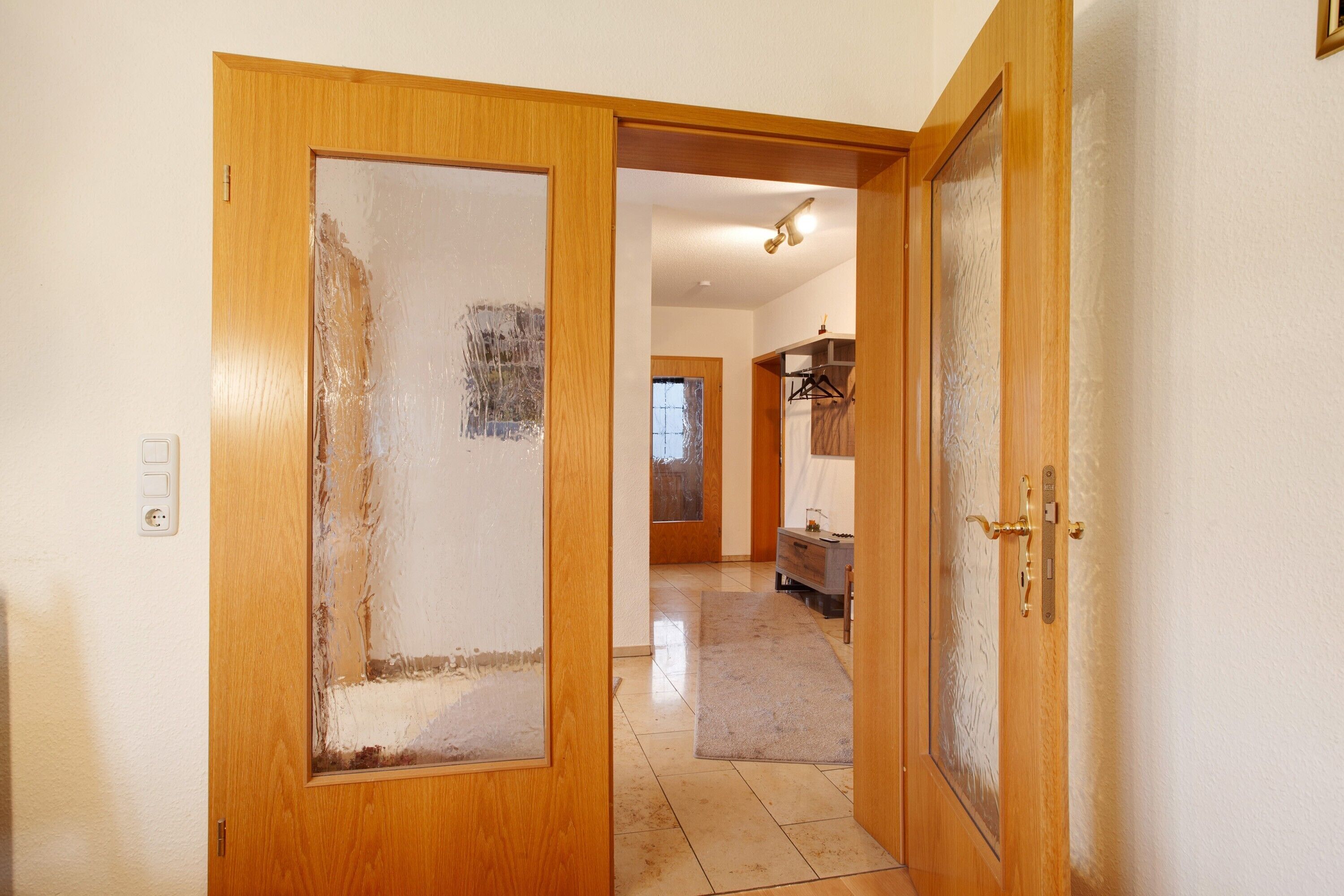 A hallway with a wooden door, a light switch, and a tiled floor.