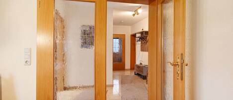 A hallway with a wooden door, a light switch, and a tiled floor.