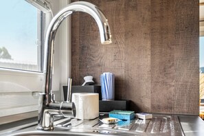 A bathroom sink with a chrome faucet, a tissue roll, a blue sponge, and a small box of toiletries.
