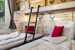 A compact room with two beds, a ladder, and a window.